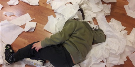Powiększ grafikę: Dziecko z głową ukrytą w ścinkach papieru