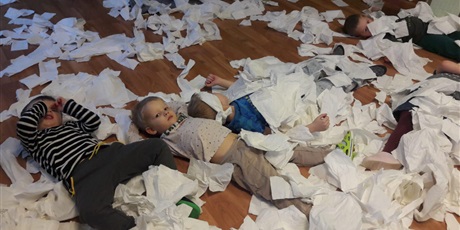 Powiększ grafikę: Sala zabaw pokryta cała białym papierem A na nich dzieci leżące na plecach.